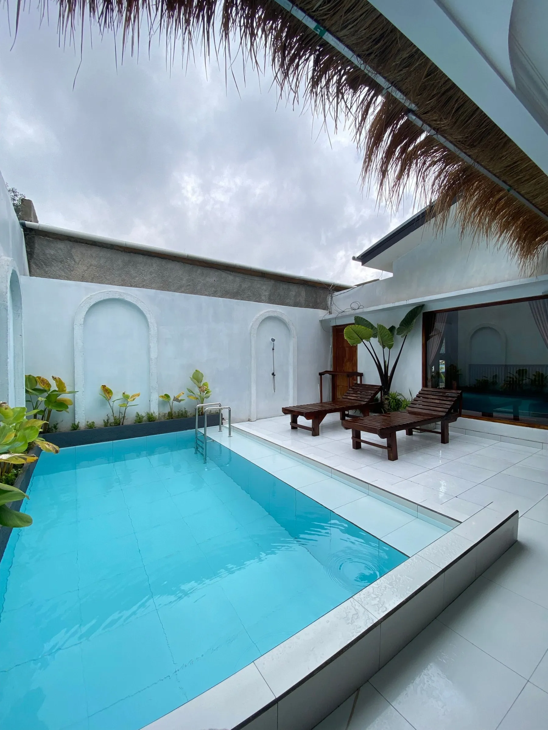 Halaman belakang rumah putih dengan kolam renang dan atap jerami